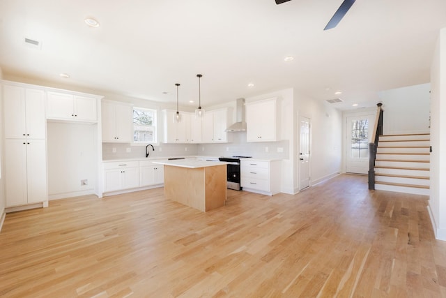 kitchen featuring light wood-type flooring, a kitchen island, electric stove, and wall chimney range hood