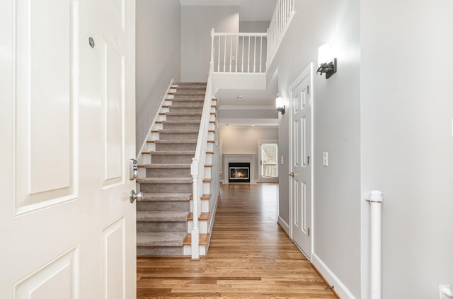 entrance foyer with stairway, baseboards, a towering ceiling, a glass covered fireplace, and light wood-type flooring