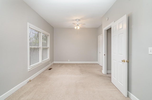 spare room featuring light carpet, a ceiling fan, and baseboards