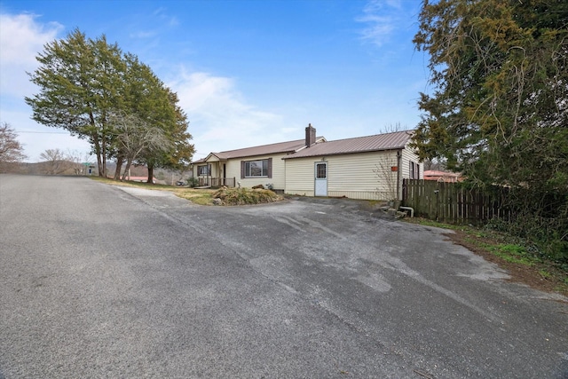 view of front of home with a chimney, driveway, metal roof, and fence