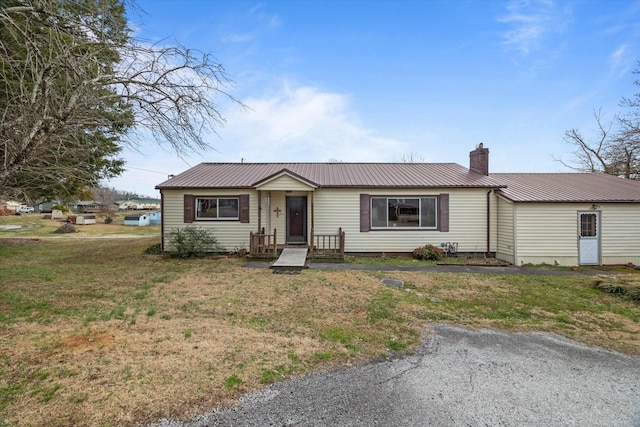 single story home with a chimney, metal roof, and a front lawn