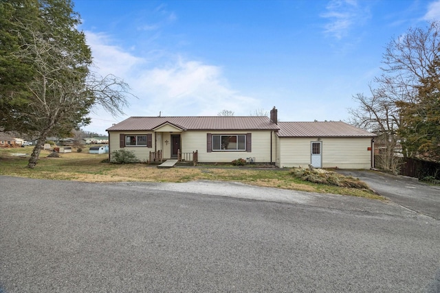 single story home with a chimney, driveway, metal roof, and a front yard