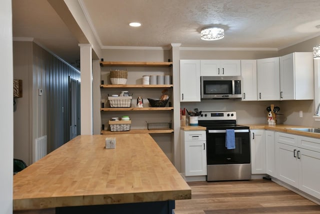 kitchen with butcher block countertops, appliances with stainless steel finishes, light wood-style flooring, and ornamental molding