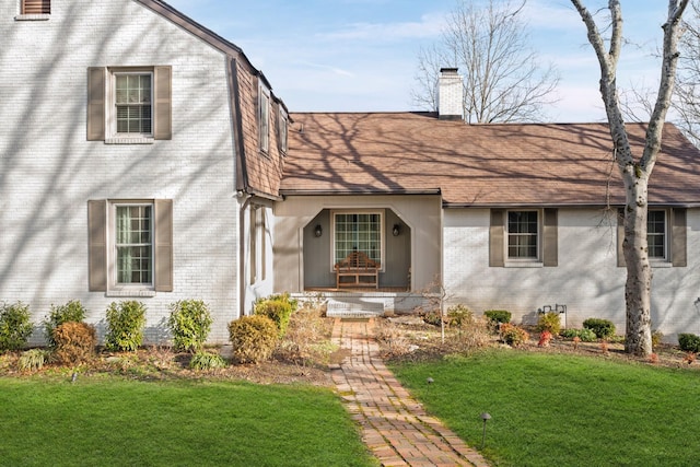 view of front of home featuring brick siding, a chimney, and a front yard