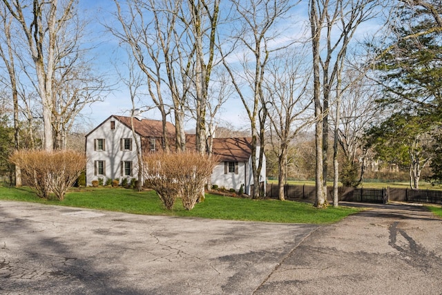 view of front facade with a gambrel roof, a front yard, and fence