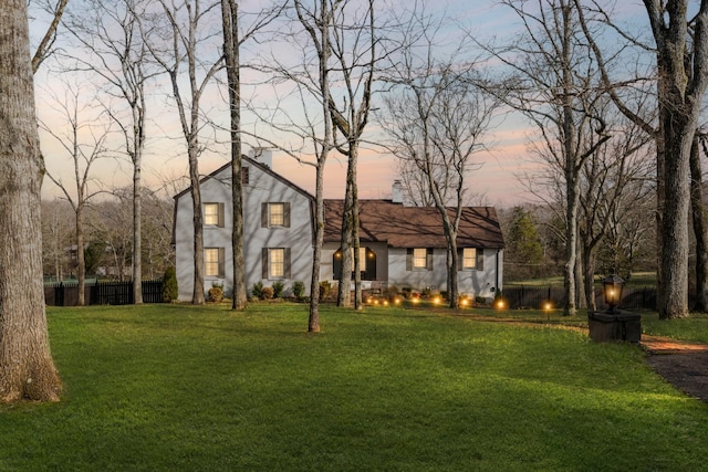 view of front facade featuring a gambrel roof, a lawn, a chimney, and fence