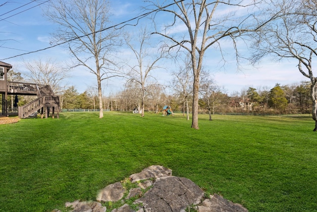 view of yard featuring playground community, a deck, and stairs