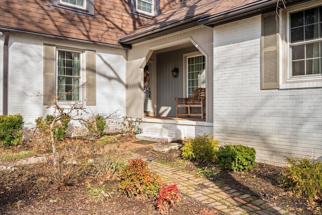 doorway to property featuring brick siding, covered porch, and a shingled roof