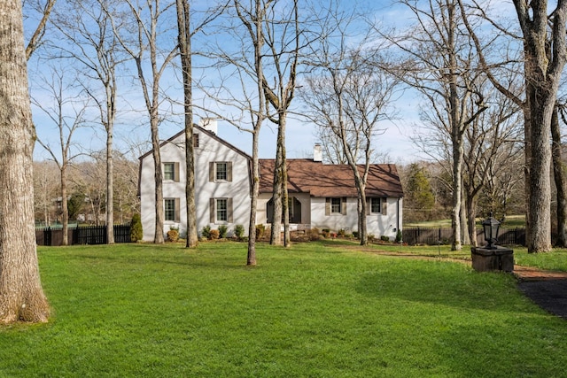 view of front facade with a chimney, a front lawn, and fence