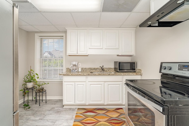 kitchen featuring under cabinet range hood, a drop ceiling, stainless steel appliances, white cabinetry, and a sink