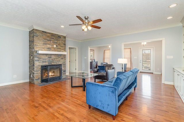 living area with a stone fireplace, light wood-style flooring, baseboards, and a textured ceiling