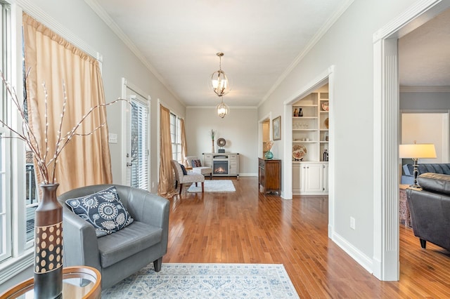 living area featuring a chandelier, baseboards, wood finished floors, and ornamental molding