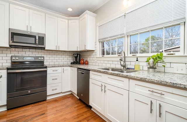 kitchen with light wood-style flooring, a sink, decorative backsplash, stainless steel appliances, and white cabinets