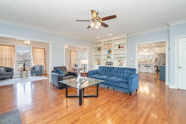 living area with crown molding, ceiling fan with notable chandelier, light wood finished floors, and a textured ceiling