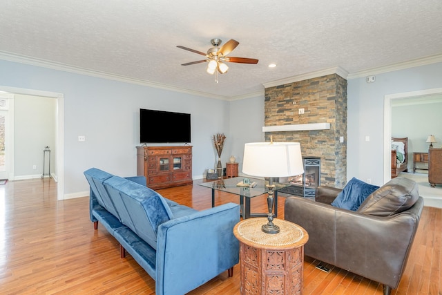 living room with light wood-style flooring, a textured ceiling, a stone fireplace, crown molding, and baseboards