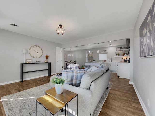 living area featuring a chandelier, visible vents, baseboards, and wood finished floors