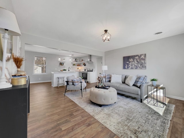 living area featuring a chandelier, visible vents, baseboards, and wood finished floors