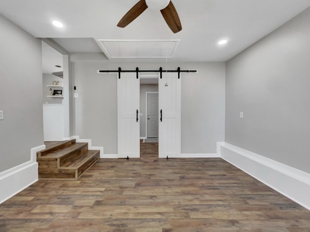 spare room with a ceiling fan, wood finished floors, baseboards, attic access, and a barn door