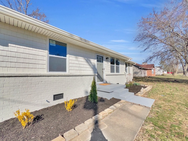 view of side of home with a lawn, brick siding, and crawl space