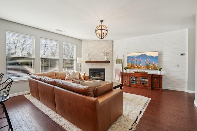 living room with visible vents, a stone fireplace, baseboards, a chandelier, and dark wood-style flooring