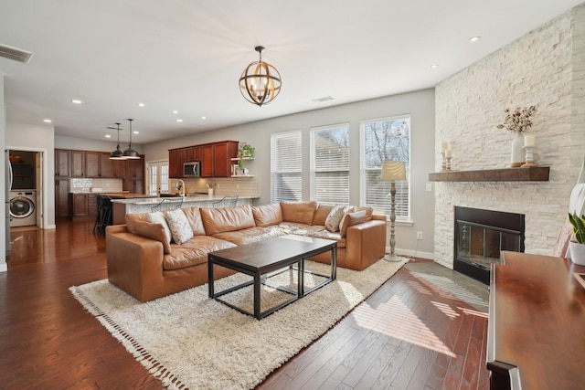 living room with washer / clothes dryer, an inviting chandelier, a fireplace, and dark wood-style flooring