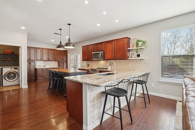 kitchen with stainless steel microwave, a healthy amount of sunlight, a breakfast bar, washer / dryer, and a sink