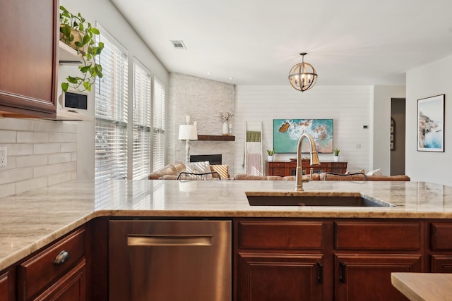 kitchen with light stone counters, stainless steel dishwasher, an inviting chandelier, and a sink