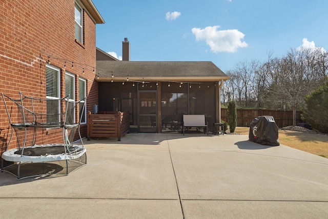 view of patio featuring a trampoline, fence, and a sunroom