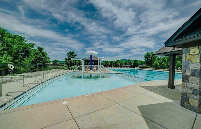 community pool with a patio, fence, and a water play area