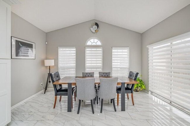 dining space featuring baseboards, lofted ceiling, and marble finish floor