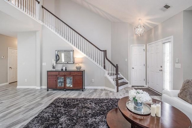 entrance foyer with visible vents, stairs, a high ceiling, and wood finished floors