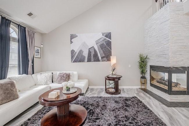 living area with visible vents, a multi sided fireplace, high vaulted ceiling, and baseboards