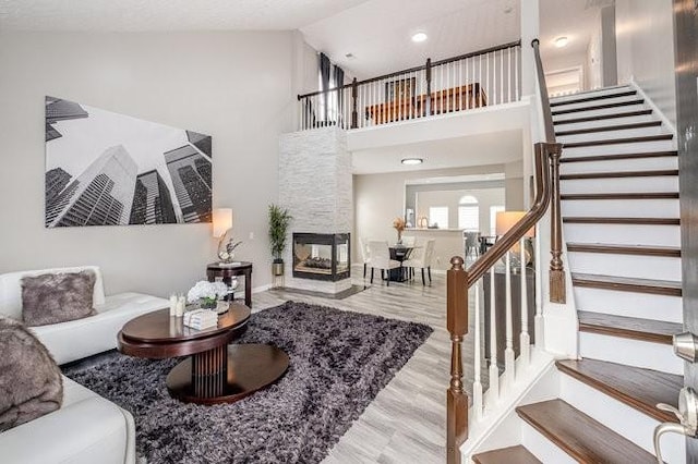 living area featuring high vaulted ceiling, stairway, a stone fireplace, and wood finished floors