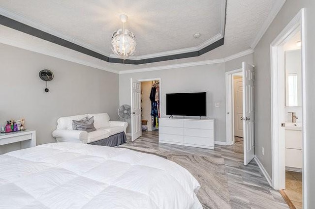 bedroom featuring a raised ceiling, a textured ceiling, crown molding, baseboards, and a spacious closet