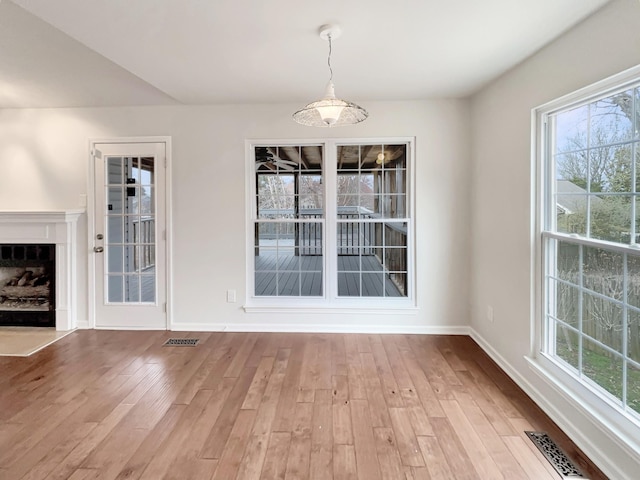 unfurnished dining area featuring a fireplace with flush hearth, wood finished floors, visible vents, and baseboards