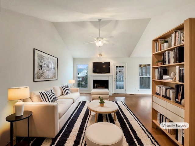 living area featuring vaulted ceiling, a fireplace, a ceiling fan, and wood finished floors