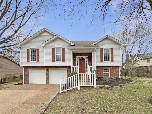 split foyer home featuring a garage, fence, brick siding, and driveway