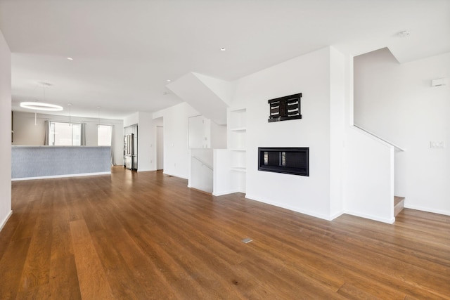 unfurnished living room with baseboards, built in shelves, dark wood-type flooring, and a glass covered fireplace