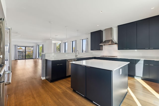 kitchen featuring a kitchen island, a peninsula, a sink, stainless steel dishwasher, and wall chimney range hood