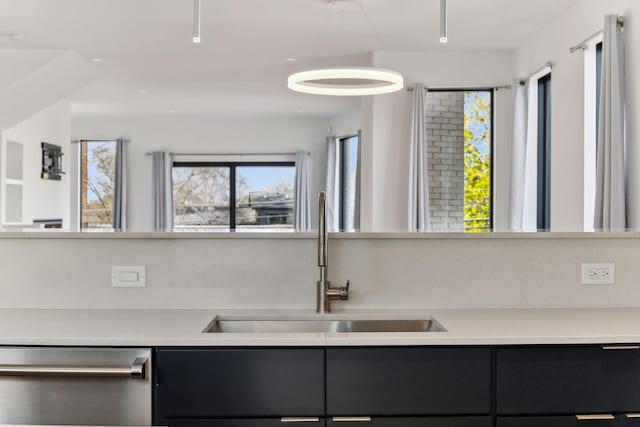 kitchen featuring stainless steel dishwasher, dark cabinetry, light countertops, and a sink