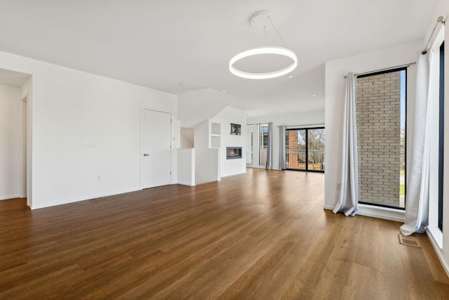 unfurnished living room featuring a glass covered fireplace, baseboards, visible vents, and wood finished floors