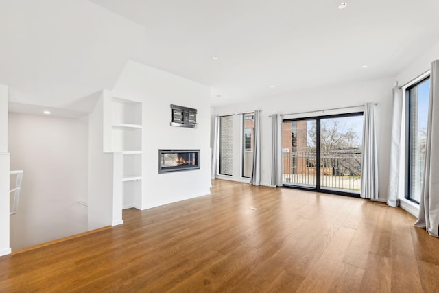 unfurnished living room featuring a glass covered fireplace, built in shelves, wood finished floors, and recessed lighting