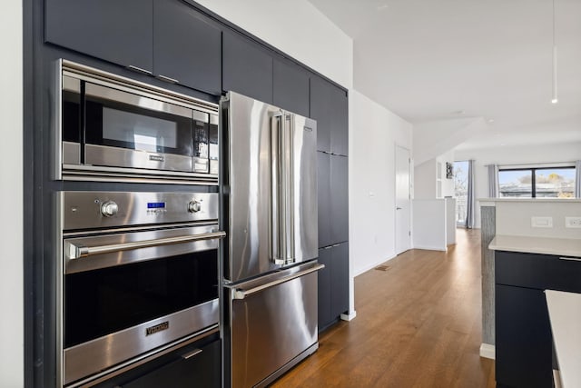 kitchen with modern cabinets, dark cabinetry, appliances with stainless steel finishes, light countertops, and dark wood-style flooring