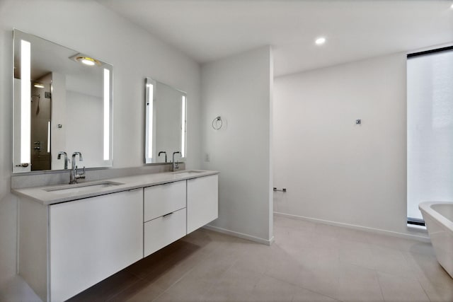 full bathroom with double vanity, a freestanding tub, baseboards, and a sink