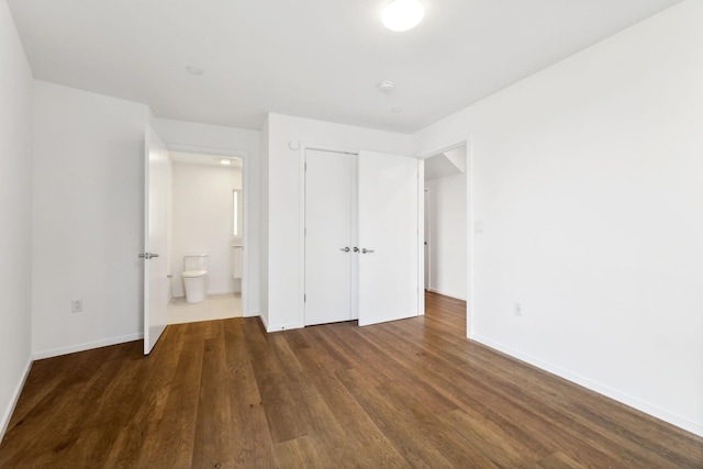 unfurnished bedroom featuring a closet, baseboards, wood finished floors, and ensuite bathroom