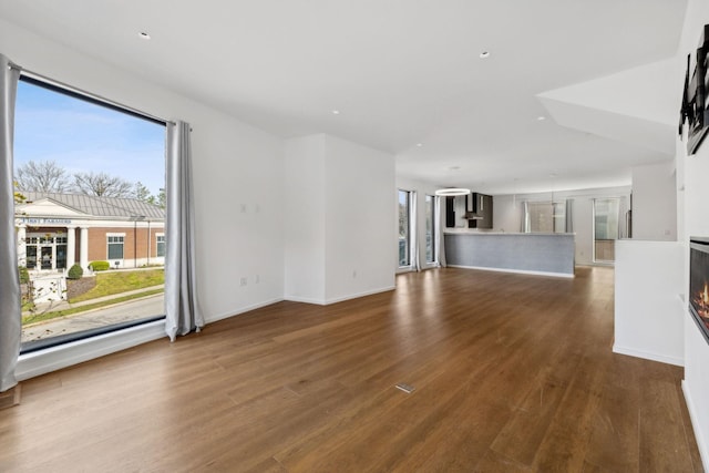 unfurnished living room with dark wood finished floors, baseboards, and a multi sided fireplace