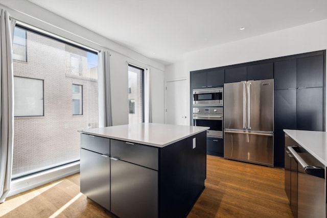 kitchen featuring a center island, stainless steel appliances, dark cabinetry, modern cabinets, and dark wood-style flooring