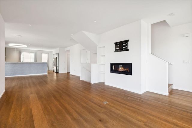 unfurnished living room featuring built in features, baseboards, a glass covered fireplace, and dark wood-style flooring