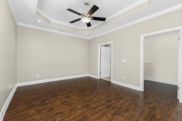 unfurnished bedroom with baseboards, dark wood-type flooring, a spacious closet, crown molding, and a raised ceiling