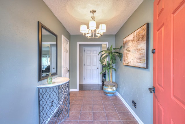 foyer entrance with a notable chandelier, baseboards, a textured ceiling, and dark tile patterned floors